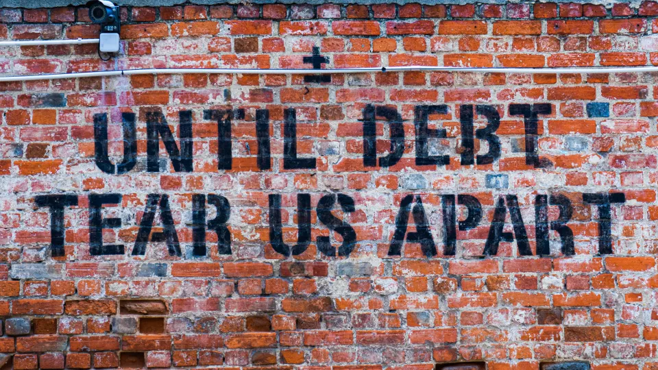 Text saying "Until debt tear us apart", printed on a red brick wall.