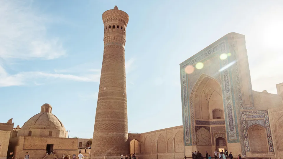 A minaret standing next to an archway in the sunshine.