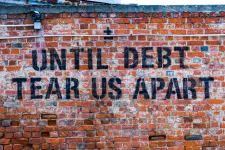 Text saying "Until debt tear us apart", printed on a red brick wall.