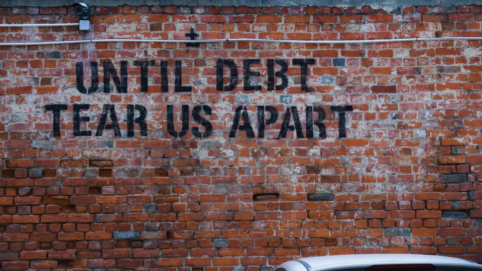 En röd tegelvägg med texten "until debt tear us apart"