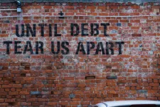 En röd tegelvägg med texten "until debt tear us apart"