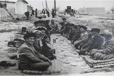 En svartvit bild på personer som sitter i en rektangelformation på marken.