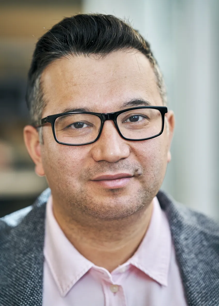 Personporträtt på en person med svart hår, glasögon och skjorta.